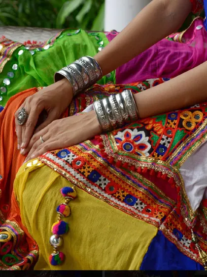 A close-up on the details: stacked silver bangles against the vibrant yellows, oranges, and reds of a traditional chaniya choli.