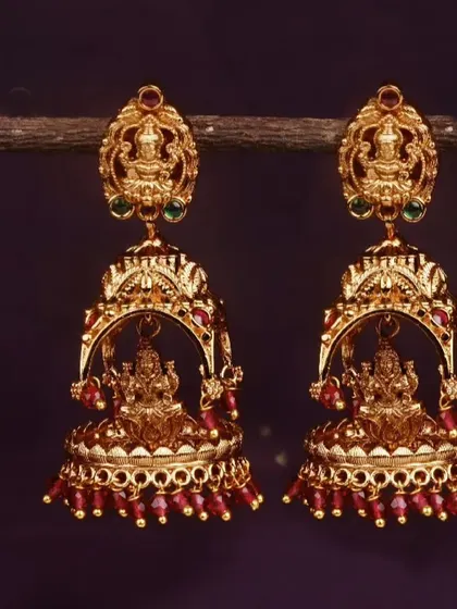 For a vibrant look, these matte gold jhumkis are available with ruby-red beads. They are perfect for brides or for adding a pop of color to a festive outfit.