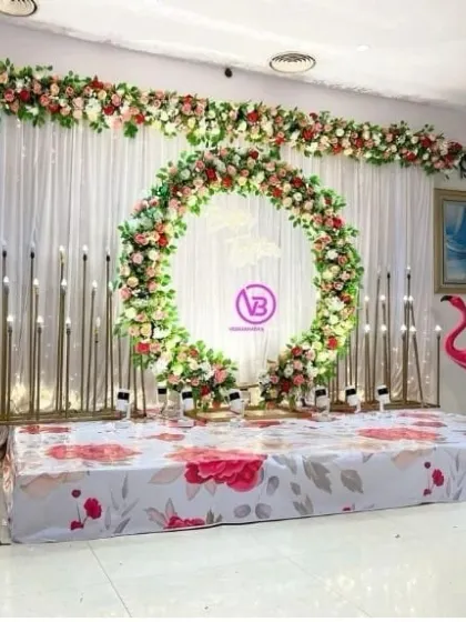 A unique floral-themed stage with a large circular wreath, a floral-printed stage floor, and fun pink flamingo props.