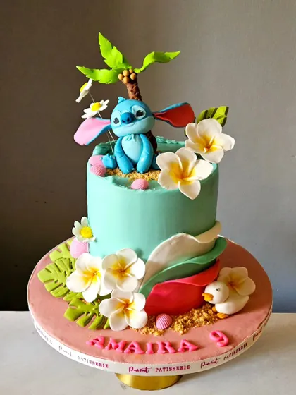 The full view of the beautiful Stitch and Hawaiian theme cake. This colored ganache cake is adorned with handmade plumeria flowers, a coconut tree, and monstera leaves.