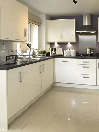A practical L-shaped kitchen with off-white glossy cabinets and a dark countertop. This is a classic, functional design that maximizes storage and workspace in a compact area.