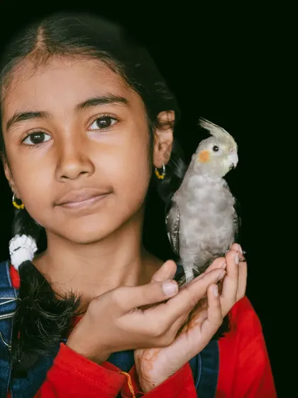 A classic portrait of a young girl holding her pet cockatiel, both looking calmly at the camera.