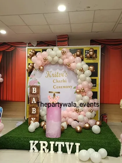 A 'Chathi Ceremony' setup with a pink and rose gold balloon arch on a grass-covered stage.