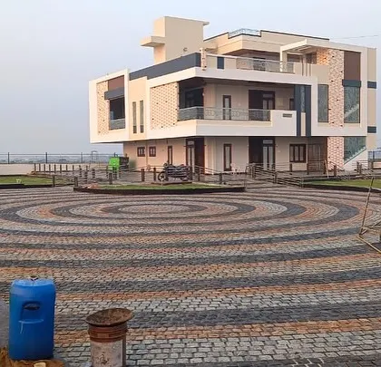A wide view of a completed project with a large, patterned cobblestone courtyard in front of a modern villa.