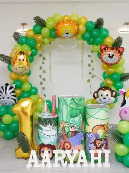 A jungle-themed first birthday party with a circular balloon arch, animal character foils, and a large '1' balloon.