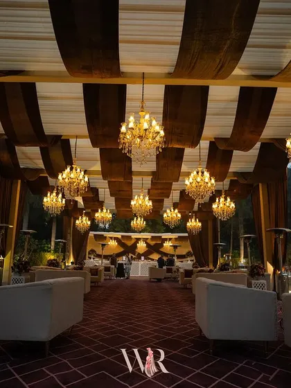Another perspective of the grand lounge tent. The symmetrical arrangement of the chandeliers and seating creates a sense of order and opulence, drawing the eye towards the back of the space.