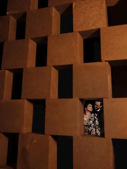 A unique and creative portrait of the couple peeking through a geometric wall, creating a playful and intimate feel for their Sangeet look.
