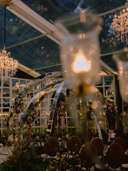 A one-of-a-kind contemporary mandap with mirrored arches, set within a massive glasshouse. This installation, surrounded by dreamy fresh florals, was designed to reflect the couple's modern personality.