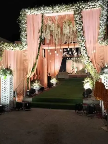A grand floral entrance for a nighttime wedding. The archway is heavily decorated with pastel pink and white flowers, with hanging chandeliers and soft draping to create a dreamy and inviting entryway.