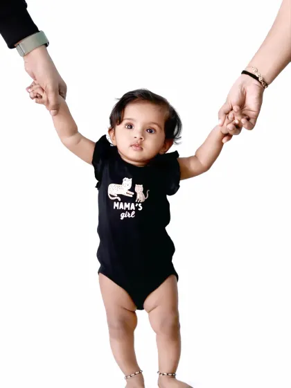 A proud 'Mama's Girl' stands with support from her parents, showing off her first steps.
