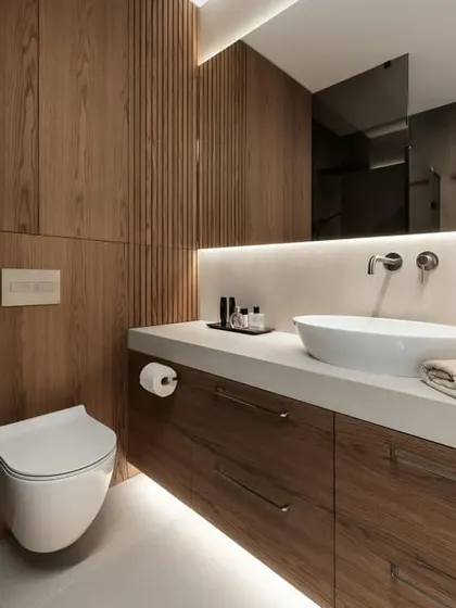 This design showcases a seamless look with a wall-mounted toilet and a floating wood vanity with a vessel sink. The back-lit mirror provides soft, ambient lighting, perfect for a relaxing bathroom.