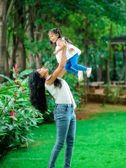 A beautiful, dynamic shot from a Mom & Me session in a park. The mother lifting her daughter into the air creates a sense of pure joy and freedom, a perfect candid moment.