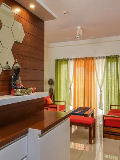 A view of a living area with bright orange traditional wooden seating. The space is defined by a custom partition featuring a display shelf with a Buddha statue and hexagonal mirror accents.