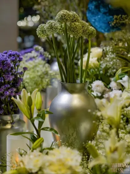 A close-up of the floral arrangements, featuring a mix of lilies, alliums, and purple statice in sleek silver vases. The details are kept modern and elegant to match the theme.