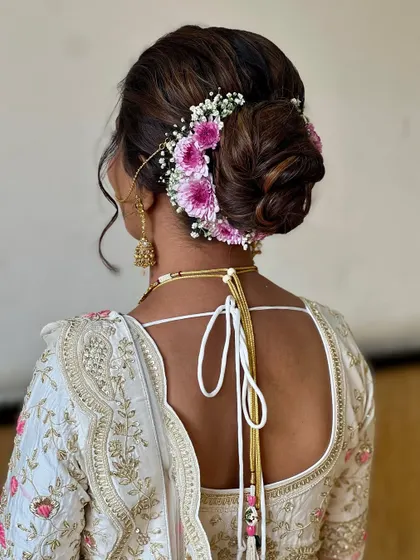 A classic bridal bun adorned with fresh pink and white flowers. This is a beautiful and traditional choice that adds a touch of freshness to the overall look.