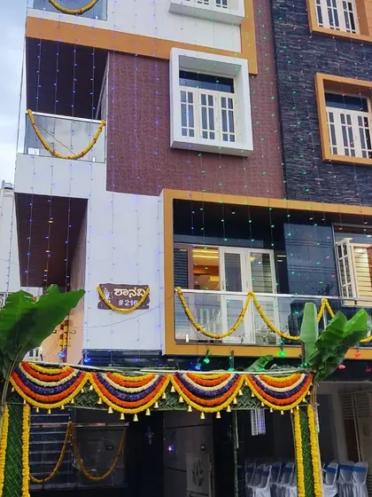 A full view of a housewarming ceremony, showing the chapra at the entrance and flower garlands decorating the balconies of the building.