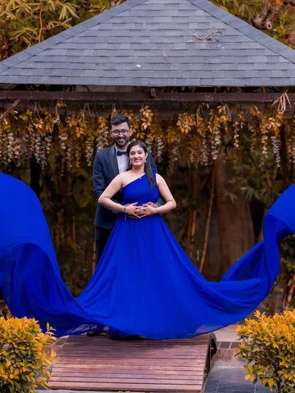 The vibrant blue gown with its flowing fabric creates a beautiful contrast against the natural bamboo and wood of the gazebo, making for a striking and stylish couple portrait.