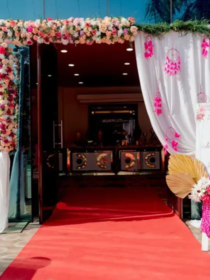 A welcoming entrance with a pastel floral theme. The archway is covered in pink and white flowers, with a red carpet leading guests into the beautifully decorated venue.