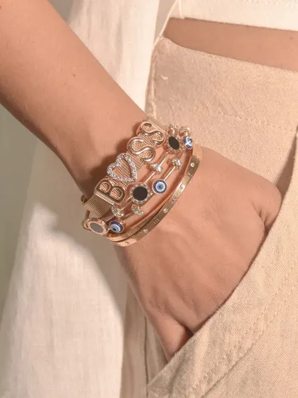A powerful 'BOSS' bracelet stack. The personalized mesh band is the star, supported by complementary evil eye and studded bangles in a matching rose gold tone.