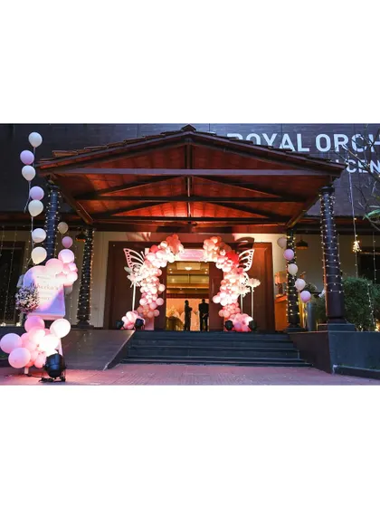 A grand entrance to a butterfly-themed party at the Royal Orchid Convention Centre, featuring a stunning pink balloon arch with large butterfly wing accents.