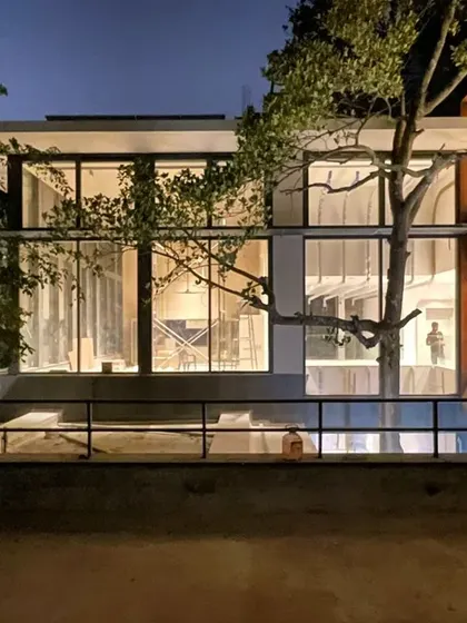 This is a glimpse of a 10,000 sqft home under construction in Koramangala. The design wraps around existing trees, with vast glass walls that dissolve the boundary between inside and out. At night, the structure glows, revealing the interplay of space, light, and nature.