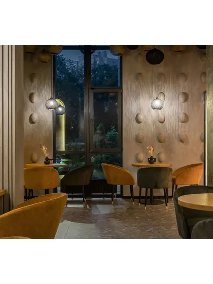 An intimate seating area with mustard and dark green velvet chairs. The textured walls and subtle pendant lighting create a cozy and sophisticated atmosphere for evening dining.