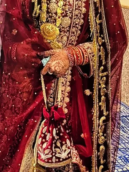 A full-length shot of a bride in her beautiful red wedding attire, with her henna-stained hands adding to the overall look.