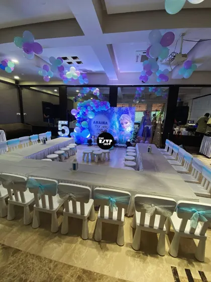 A full view of the kids' seating arrangement for a Frozen party, with long tables and chairs decorated with light blue sashes, all facing the main stage.