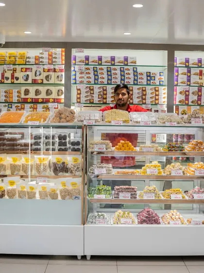 This is my sweets and namkeen counter. You can see the fresh mithai displayed in the refrigerated case to maintain its taste and quality. My staff is always ready to help you choose.