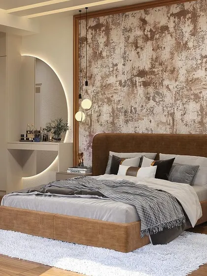 We designed this bedroom to feel both luxurious and comfortable. The space features a custom bed with a brown upholstered headboard, a rustic-textured accent wall, and a floating dresser with a backlit circular mirror.