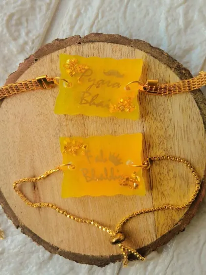 A custom resin rakhi and lumba set for bhaiya and bhabhi, made with a vibrant yellow color and gold flakes.