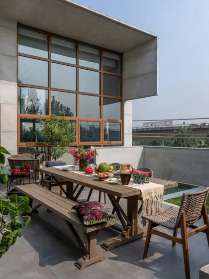 The outdoor dining area of the Dhaka residence, set against the home's modern concrete and glass facade. This space was designed for leisurely meals and entertaining, connecting the interior living areas with the garden and pool.