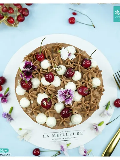 A classic Black Forest cake, generously decorated with fresh cherries, chocolate frosting, and dollops of fresh cream. It's a timeless choice for any celebration.