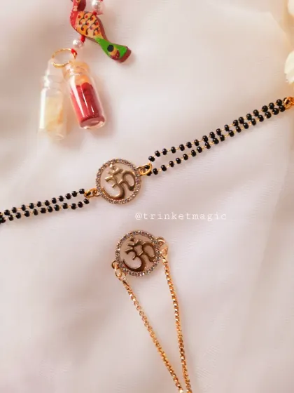 This set blends tradition with modern spirituality. The Om symbol is set in a crystal-studded circle on a mangalsutra-style bracelet for bhabhi and a matching chain Rakhi for bhai.