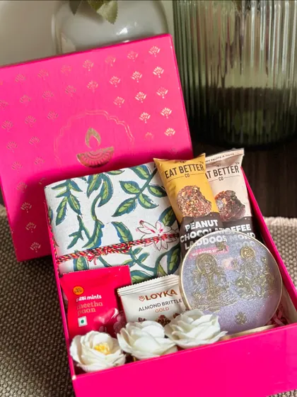 A compact and pretty pink Diwali box, including a handcrafted notebook, a Ganesh and Laxmi resin stand, and sweet treats.