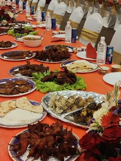 A beautiful spread on a long dining table, decorated with floral arrangements. Platters of fried quail, fish, and chicken are laid out, ready for a wedding reception.