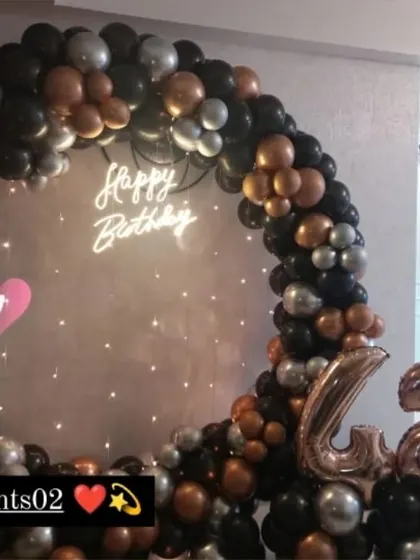 A stylish setup for a 42nd birthday, featuring a black, bronze, and silver balloon ring against a textured wall, complete with rose gold number balloons.