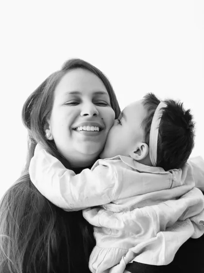 A black and white photo of a baby giving her smiling mother a kiss on the cheek.