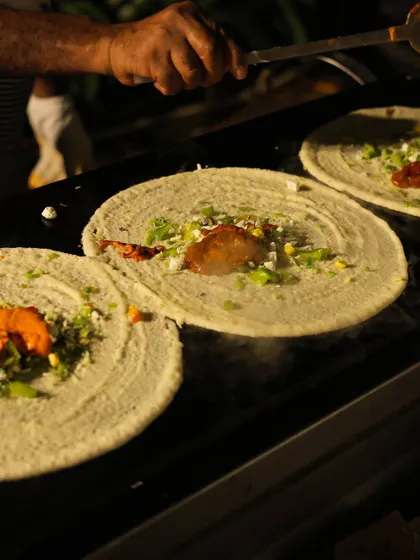 My team ensures every dosa is made to perfection, even during the busiest events. Here, a chef spreads the spicy filling evenly across three dosas cooking on the griddle.