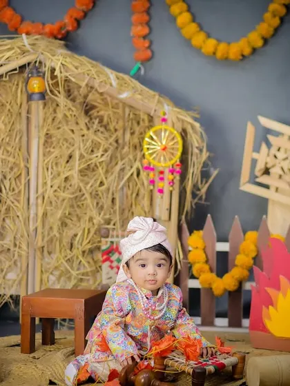 A full view of the Lohri setup, showing the baby sitting near the bonfire and charpai, surrounded by colorful props that celebrate Punjabi culture.