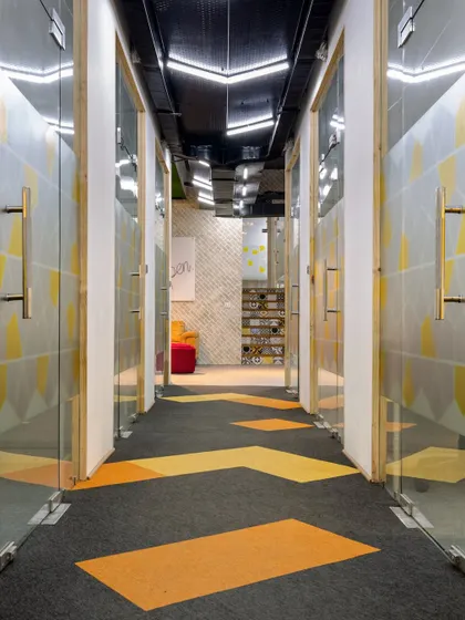 The corridor is brought to life with geometric patterns on the carpet tiles and walls. This design choice creates a sense of movement and visual continuity, connecting the different zones of the office in a dynamic way.