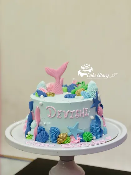 An underwater adventure with this mermaid-themed cake. The light blue cake is decorated with a pink mermaid tail and a variety of colorful fondant seashells and starfish.