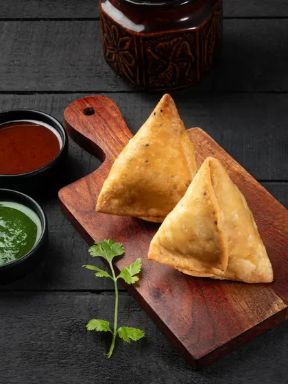 This shot of samosas uses dramatic, directional lighting to emphasize their crispy, golden-brown texture. The dark background makes them the undisputed hero of the frame.