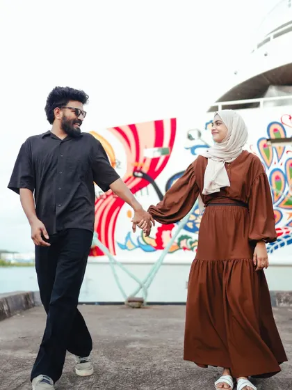 The couple walks hand-in-hand along a pier, their casual outfits and happy expressions creating a relaxed and joyful pre-wedding photo.
