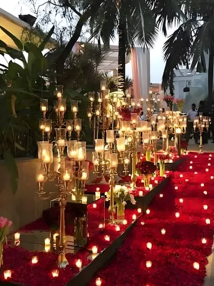 A breathtaking pathway lined with golden candelabras and a carpet of red rose petals. The mirrored floor reflects the candlelight, creating an infinitely romantic and dramatic entrance.