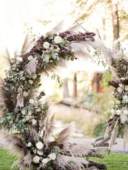 A beautiful and rustic circular wedding arch made from twigs and decorated with pampas grass and white roses, perfect for a bohemian or garden wedding.