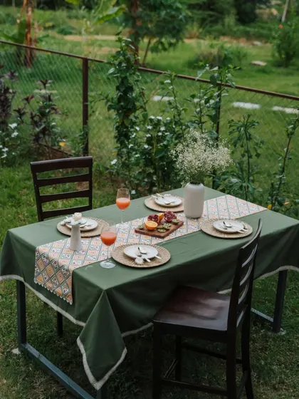 An outdoor dining scene featuring our solid green tablecloth and a patterned runner. This combination creates a lush, garden-inspired look that is both sophisticated and welcoming.