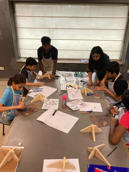 A group of young artists focused on their woodcut projects. I guide them in sketching their ideas and safely using carving tools to bring their designs to life on the woodblocks before they head to the printing press.