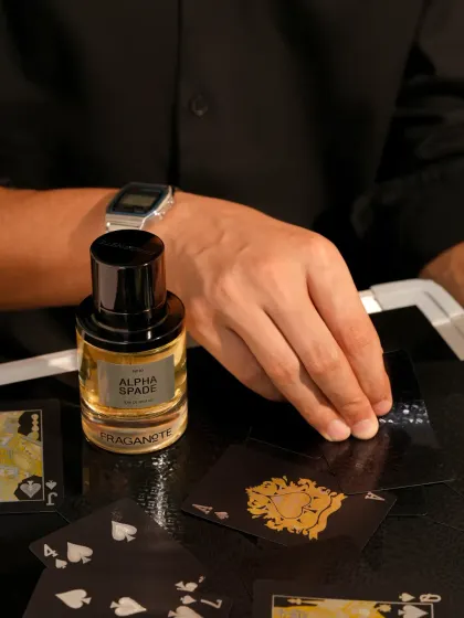 A lifestyle shot for a men's fragrance, featuring a hand model dealing cards. This places the product in an aspirational context of sophistication and gamesmanship.