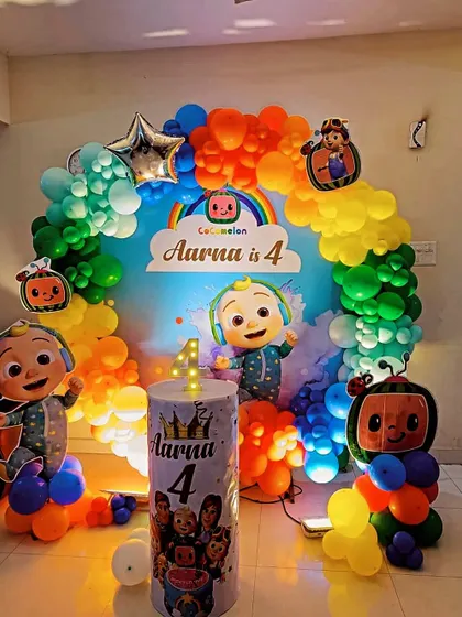 A vibrant Cocomelon theme for a 4th birthday, featuring a rainbow balloon arch over a custom backdrop and character standees.